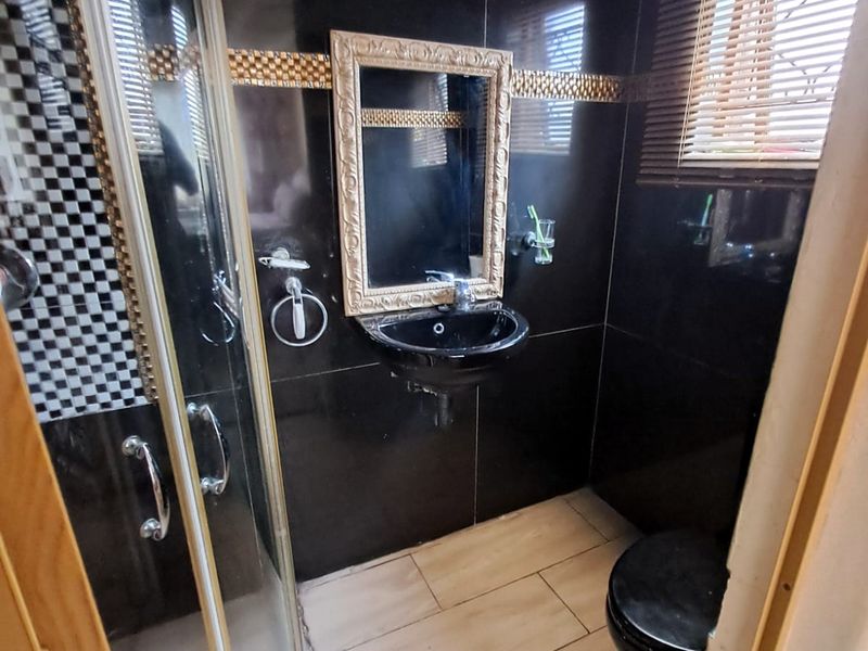 A compact bathroom featuring black wall tiles, a corner shower enclosure, a wall-mounted basin, and a toilet with wood-look floor tiling.