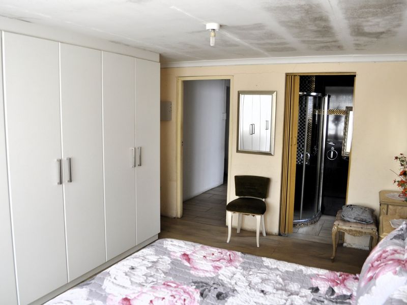 Bedroom featuring built-in cupboards and an en-suite bathroom with a shower cubicle. The ceiling shows signs of water damage and requires repair.