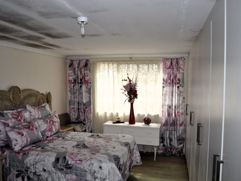 A bedroom featuring built-in cupboards and laminate flooring, currently showing significant water damage and staining on the ceiling.