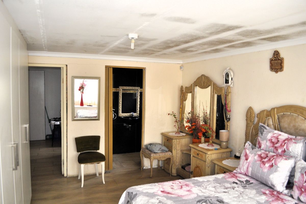 Spacious bedroom featuring laminate flooring, built-in wardrobe, and direct access to an en-suite bathroom. Note visible ceiling water damage requiring attention.
