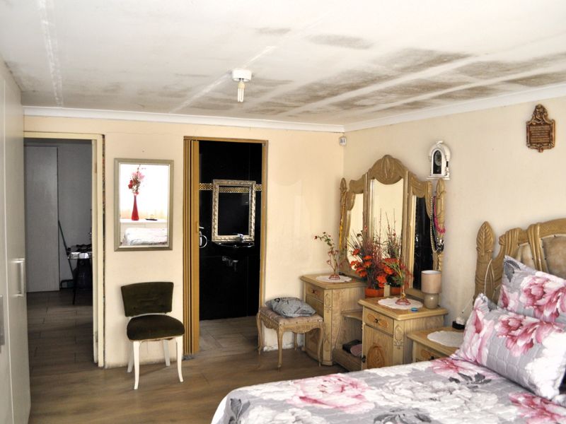 Spacious bedroom featuring laminate flooring, built-in wardrobe, and direct access to an en-suite bathroom. Note visible ceiling water damage requiring attention.