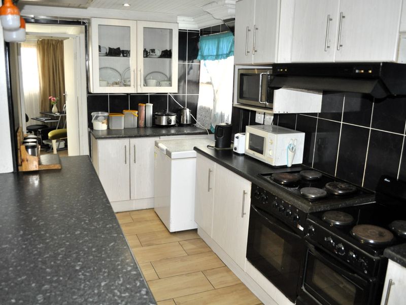 A functional kitchen featuring white cabinetry, black tiled backsplash, dark countertops, and built-in cooking appliances with tiled flooring throughout.