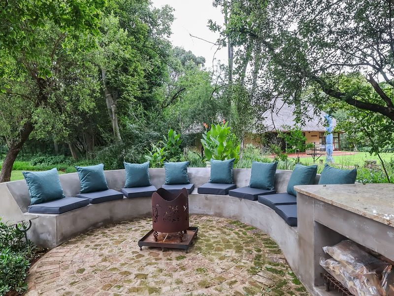 Outdoor garden area featuring a curved concrete bench, stone paved patio, built-in stone countertop, and a central fire pit set within a lush landscape.
