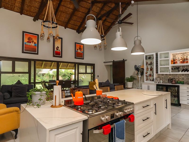 Spacious open-plan kitchen and living area featuring a large island with gas hob, custom cabinetry, wine cooler, and high vaulted thatched ceilings with exposed beams.