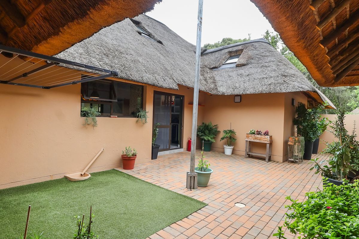 A private rear courtyard featuring brick paving, a section of artificial grass, and a traditional thatch roof structure with integrated skylights.