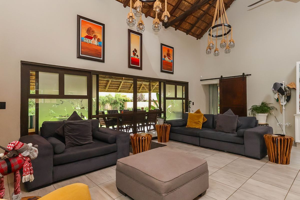 Spacious living room featuring a high vaulted thatched ceiling, large sliding glass doors opening to the patio, and neutral tiled flooring.