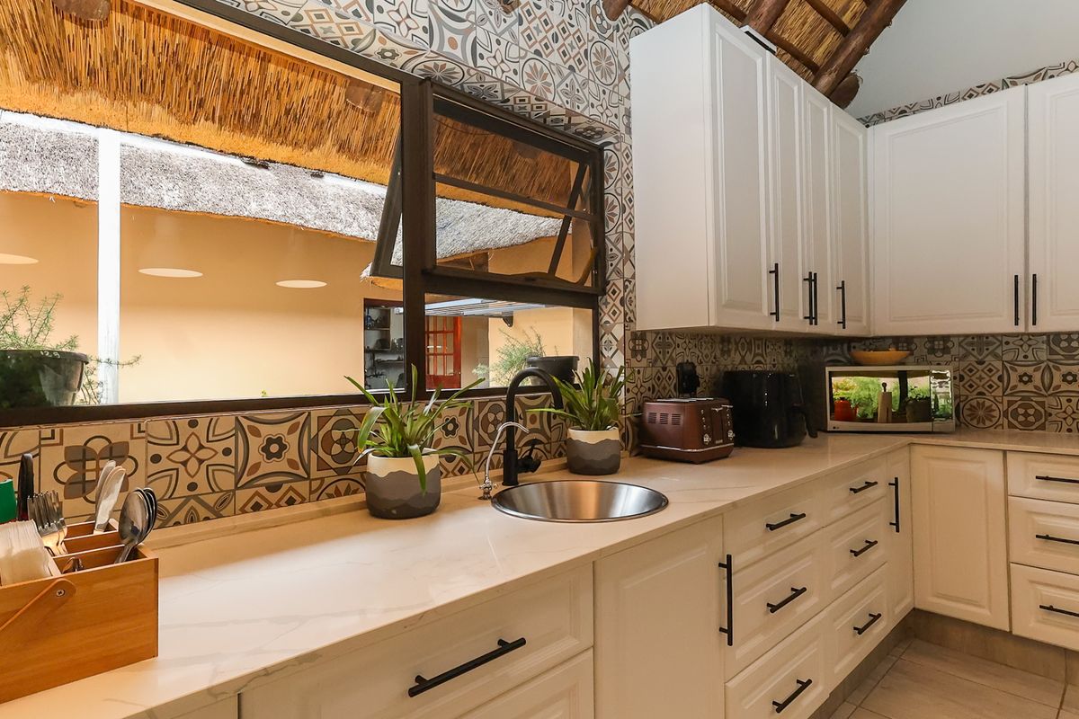 A well-maintained kitchen featuring white cabinetry, stone countertops, a modern undermount sink, and decorative patterned tile backsplash under a unique thatched roof.