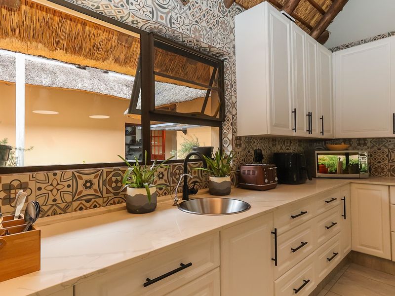 A well-maintained kitchen featuring white cabinetry, stone countertops, a modern undermount sink, and decorative patterned tile backsplash under a unique thatched roof.