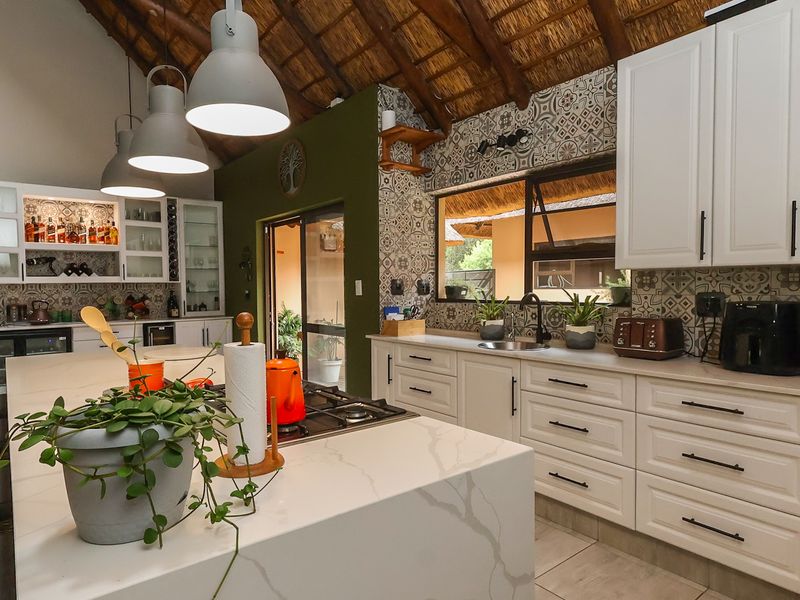 A spacious kitchen featuring a large island with a gas hob, white cabinetry, decorative tiled backsplash, and a high vaulted thatch ceiling.