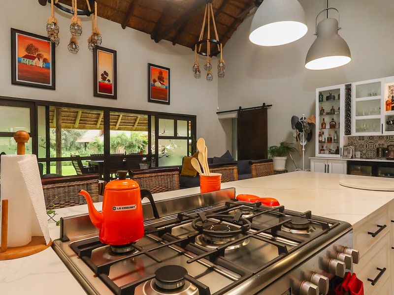 Spacious open-plan kitchen and living area featuring a large central island with gas cooktop, high thatched ceilings, and seamless flow to the outdoor patio.