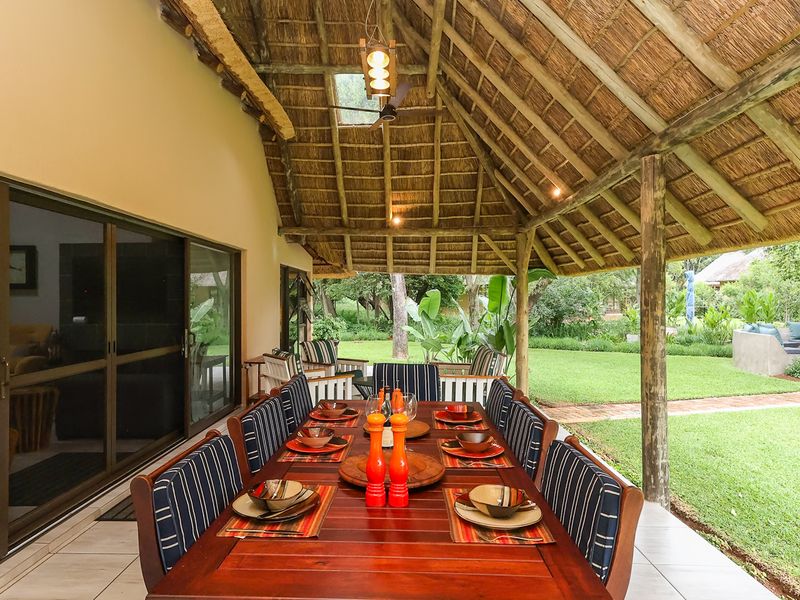 Spacious covered patio featuring a traditional thatched roof, exposed timber rafters, and large sliding glass doors opening onto a lush garden.