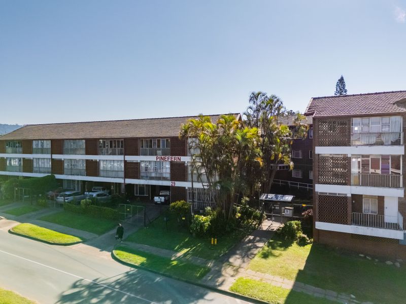 Aerial view of the Pinefern apartment complex, featuring a multi-story brick facade, tiled roofing, and established garden surroundings.