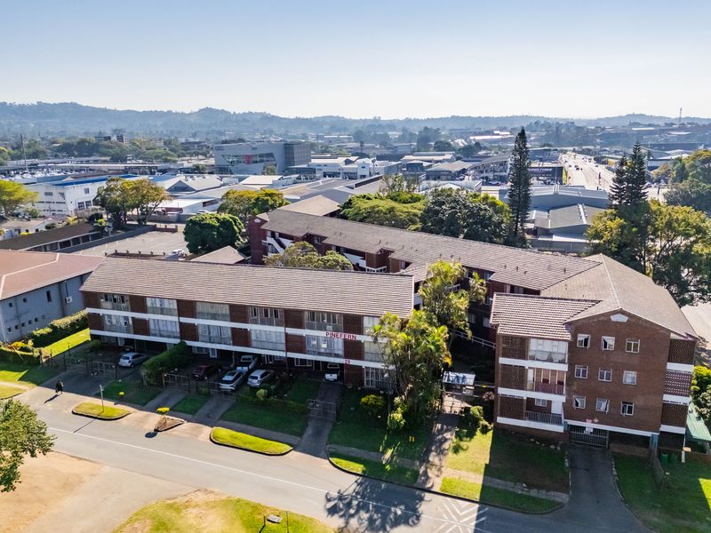 Aerial view of the Pinefern apartment complex, showcasing the brick building structure, tiled roofing, and surrounding neighborhood context.