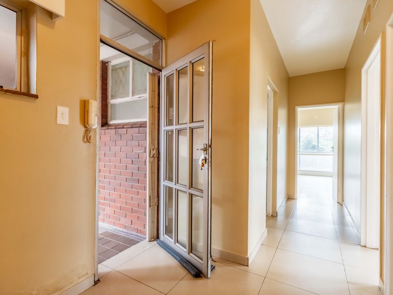 Entrance hallway featuring tiled flooring and a glass panelled security door, leading into the apartment interior.