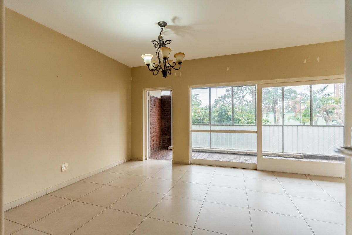 An empty living room featuring tiled flooring, a central chandelier, and large sliding glass doors providing access to an outdoor balcony area.