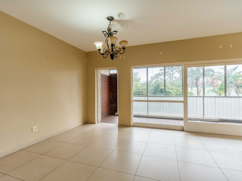 An empty living room featuring tiled flooring, a central chandelier, and large sliding glass doors providing access to an outdoor balcony area.