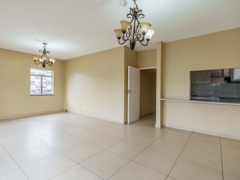 Spacious open-plan living area featuring neutral tiled flooring, decorative chandeliers, and a convenient breakfast bar pass-through to the kitchen.