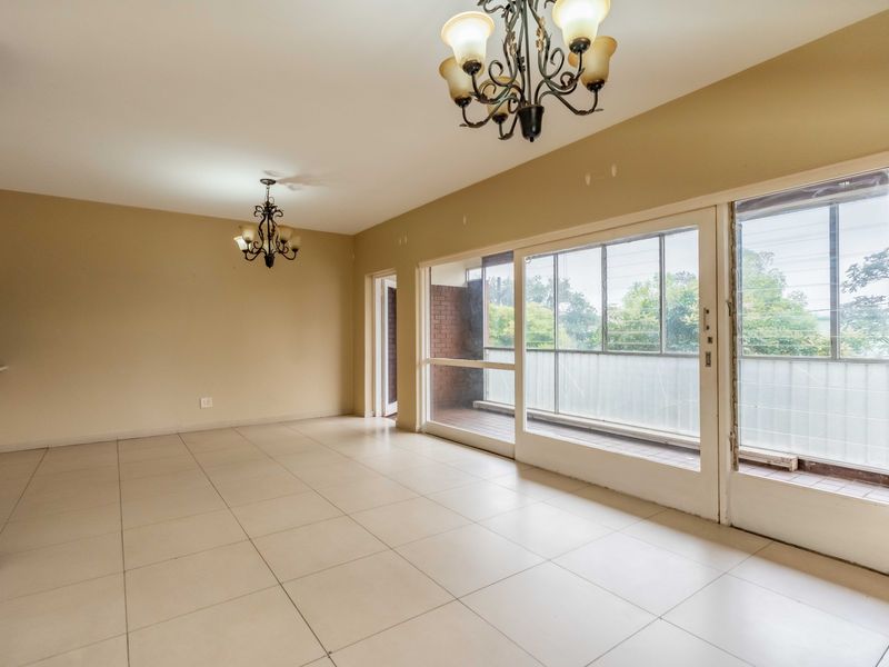 Spacious, empty living area featuring neutral tiled flooring, classic wrought iron chandeliers, and large sliding glass doors leading to an outdoor balcony.
