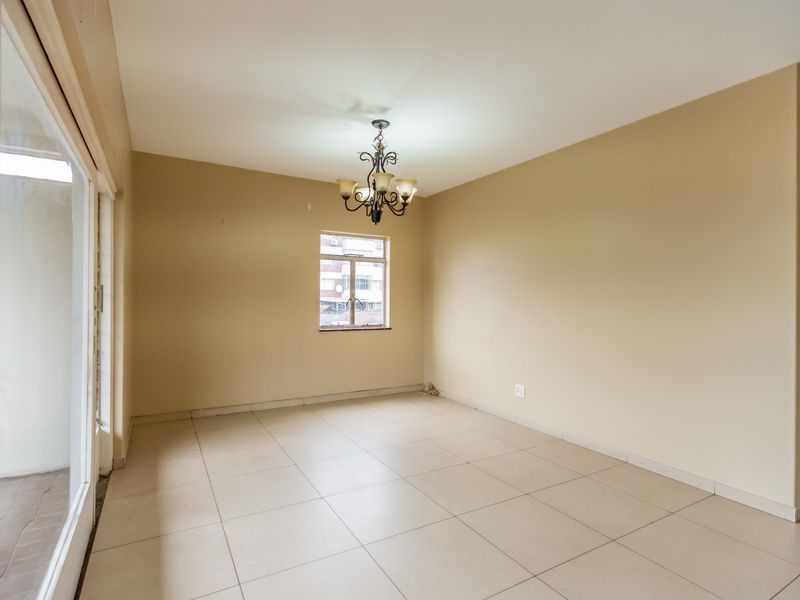 A bright, empty living area featuring neutral tiled flooring, a central chandelier, and a sliding glass door leading to an outdoor space.