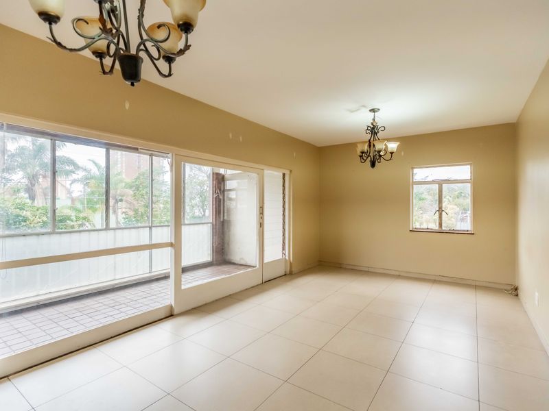 Spacious, empty living area featuring neutral tiled flooring, large sliding glass doors leading to a balcony, and natural light through multiple windows.