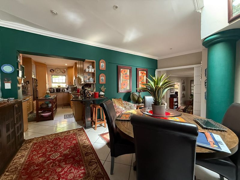 Open-plan dining and kitchen area featuring tiled floors, recessed lighting, and dark green accent walls, providing a functional and connected living space.