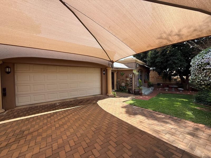Front exterior view featuring a paved driveway, a large shade sail covering the parking area, and a sectional garage door.