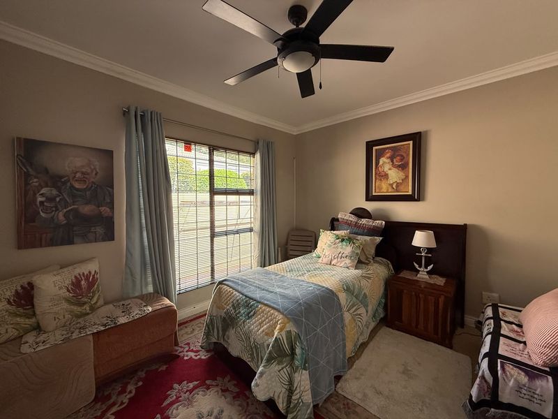 A cozy bedroom featuring a ceiling fan, cornice detailing, and window blinds, providing a comfortable and functional living space.