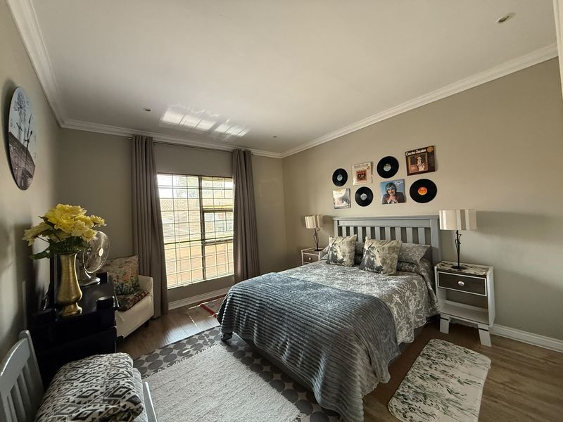A well-maintained bedroom featuring laminate flooring, coved cornicing, and recessed downlighting, with a window fitted with security bars.