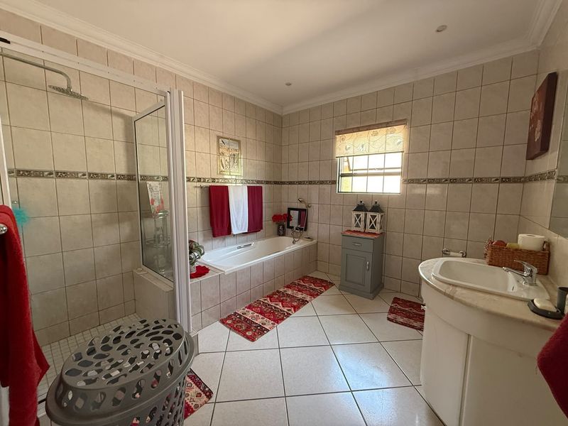 Spacious bathroom featuring a built-in bathtub, separate walk-in shower, and a vanity unit with neutral ceramic tiling throughout.