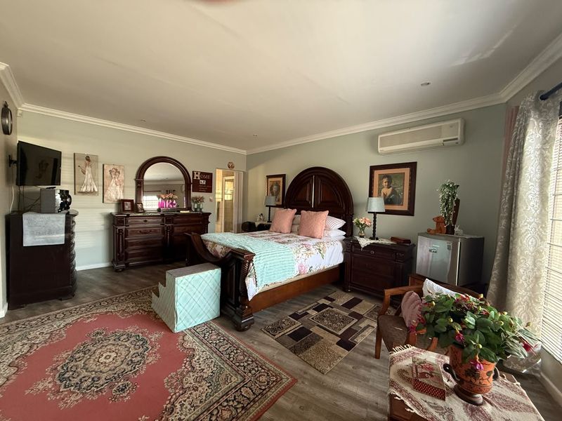 Spacious bedroom featuring laminate flooring, recessed downlighting, and a wall-mounted air conditioning unit.