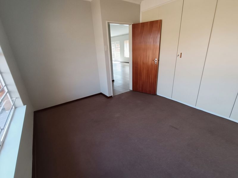 An empty bedroom featuring built-in cupboards, carpeted flooring, and a wooden door, with a view into the adjacent hallway.