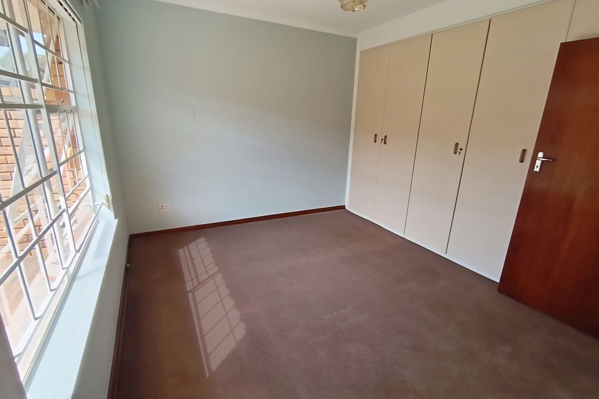 A clean, empty bedroom featuring built-in cupboards, carpeted flooring, and a window with security bars, offering a neutral space ready for personalization.
