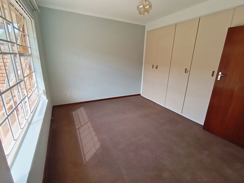 A clean, empty bedroom featuring built-in cupboards, carpeted flooring, and a window with security bars, offering a neutral space ready for personalization.