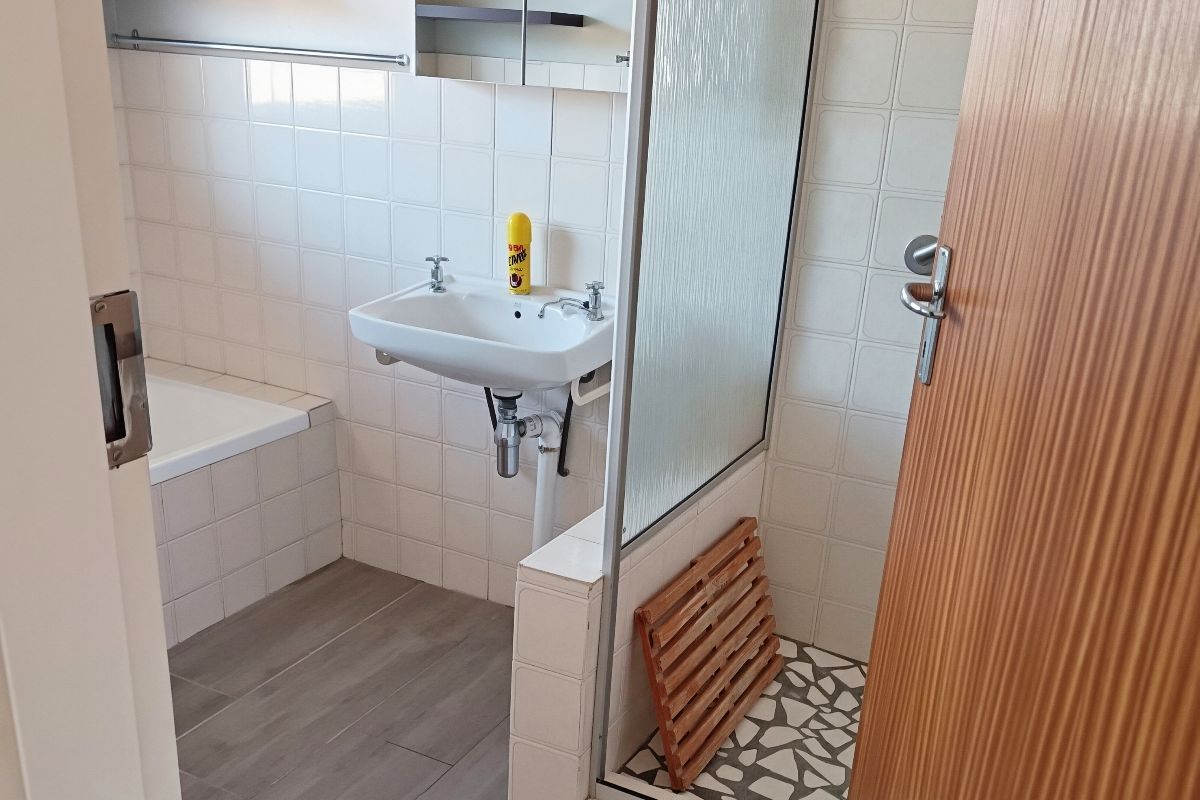 A functional bathroom featuring a built-in bathtub, a separate shower enclosure with glass screen, and a wall-mounted basin with tiled finishes.