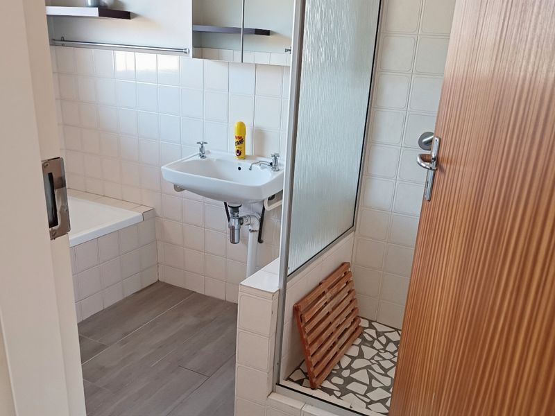 A functional bathroom featuring a built-in bathtub, a separate shower enclosure with glass screen, and a wall-mounted basin with tiled finishes.