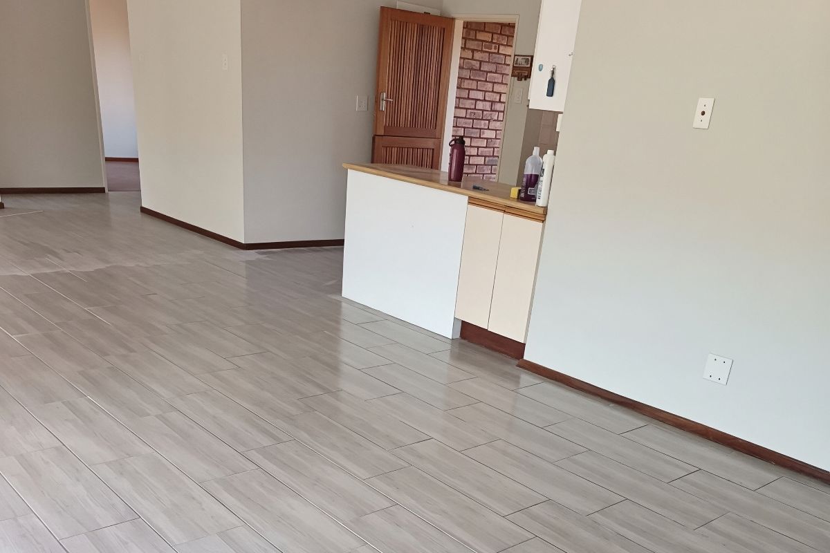 An open-plan living area featuring modern wood-look tile flooring, neutral walls, and a small built-in kitchen counter section.