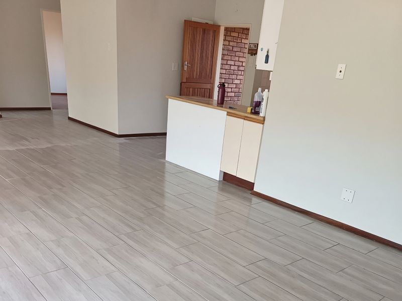 An open-plan living area featuring modern wood-look tile flooring, neutral walls, and a small built-in kitchen counter section.