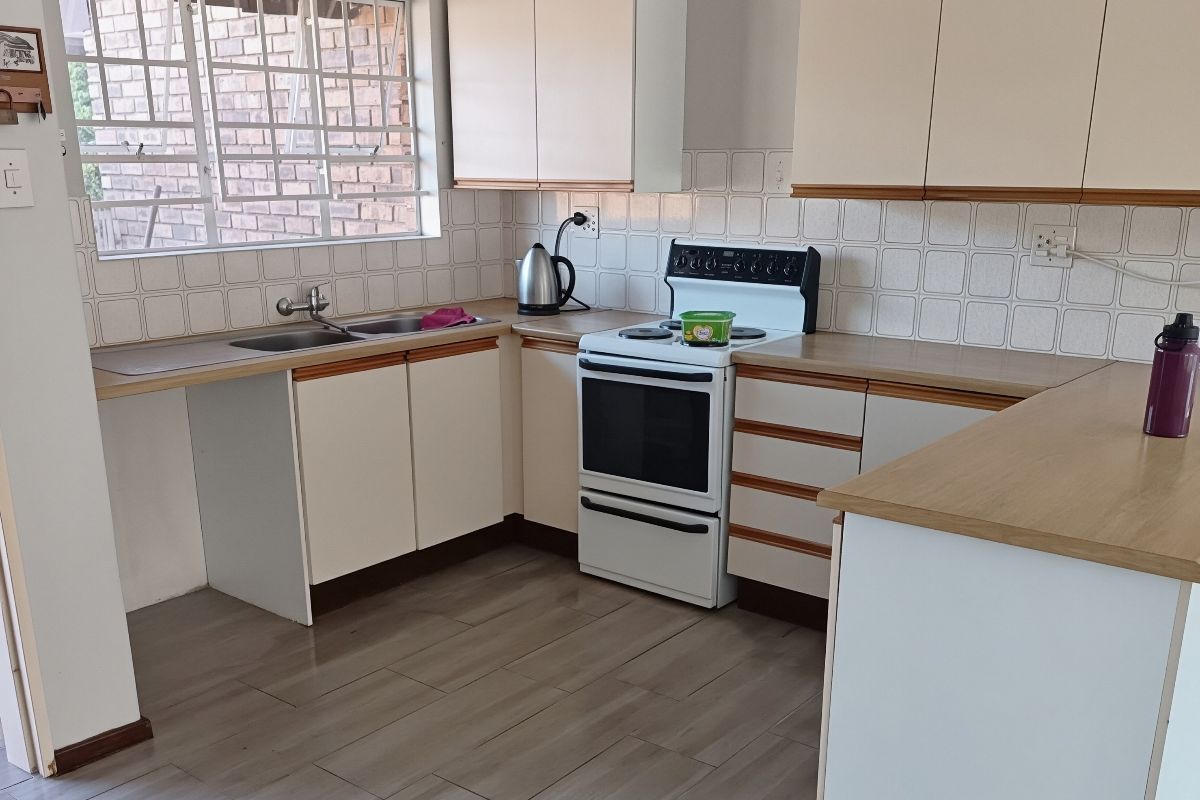 A functional kitchen featuring laminate cabinetry, wood-look countertops, a double basin sink, and a freestanding stove with tiled backsplash.