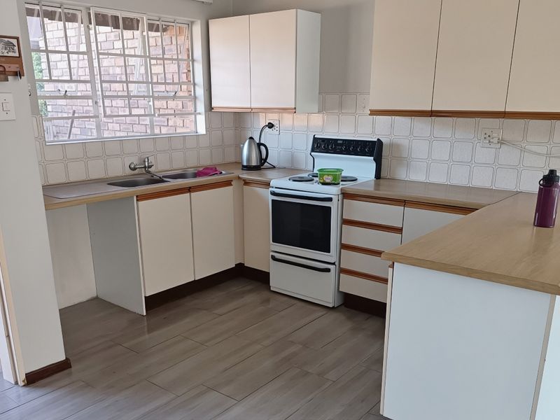 A functional kitchen featuring laminate cabinetry, wood-look countertops, a double basin sink, and a freestanding stove with tiled backsplash.