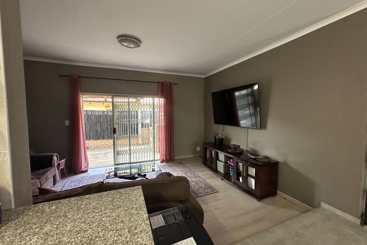 Spacious living room featuring laminate flooring, neutral wall tones, and a sliding glass door with security gate providing access to the outdoor area.