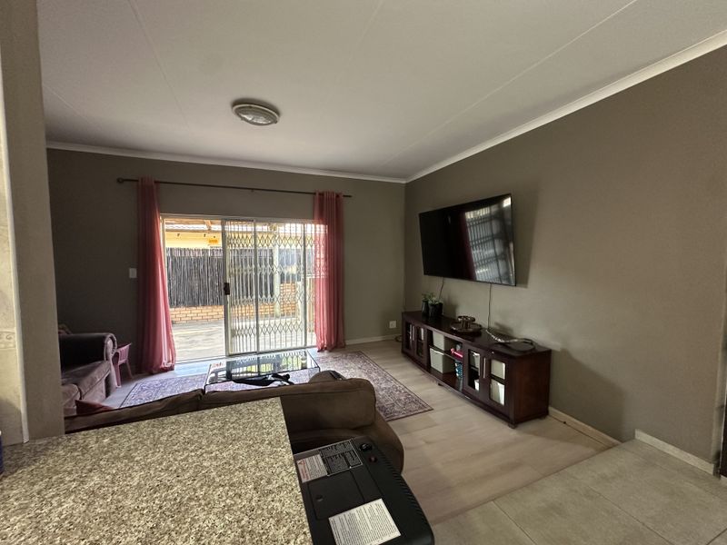 Spacious living room featuring laminate flooring, neutral wall tones, and a sliding glass door with security gate providing access to the outdoor area.