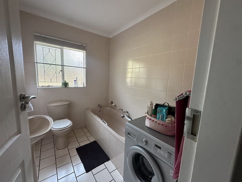 A functional bathroom featuring a bathtub, pedestal basin, and toilet with neutral wall tiling and tiled flooring.