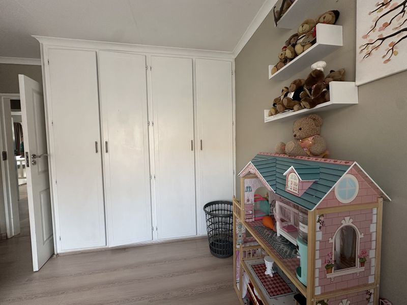 A bedroom featuring light-toned laminate flooring and white built-in cupboards providing ample storage space.