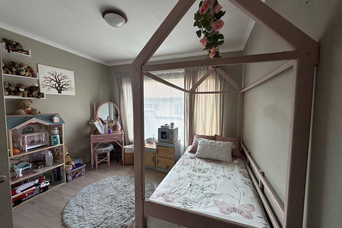 A cozy bedroom featuring laminate flooring, built-in wall shelving, and a neutral color palette, offering a functional space for a child's room.
