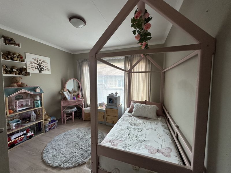 A cozy bedroom featuring laminate flooring, built-in wall shelving, and a neutral color palette, offering a functional space for a child's room.