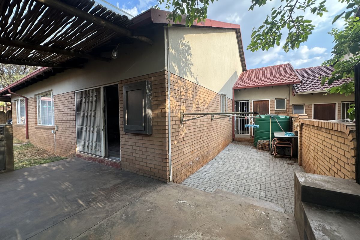 Rear exterior view featuring a brick facade, a covered patio area with a thatched roof, a paved courtyard, and a water storage tank.