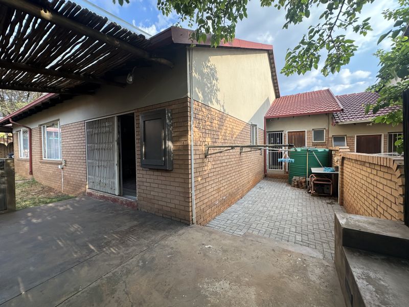 Rear exterior view featuring a brick facade, a covered patio area with a thatched roof, a paved courtyard, and a water storage tank.
