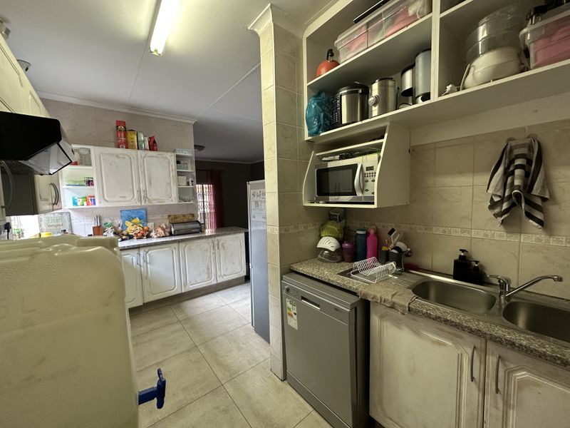 A functional kitchen featuring granite countertops, double sink, built-in cabinetry, and tiled finishes, offering potential for modernization and aesthetic updates.