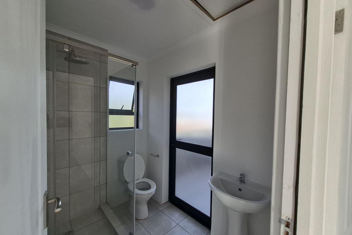 A clean, modern bathroom featuring a glass-enclosed shower, pedestal basin, and toilet, with tiled flooring and a frosted glass door for privacy.