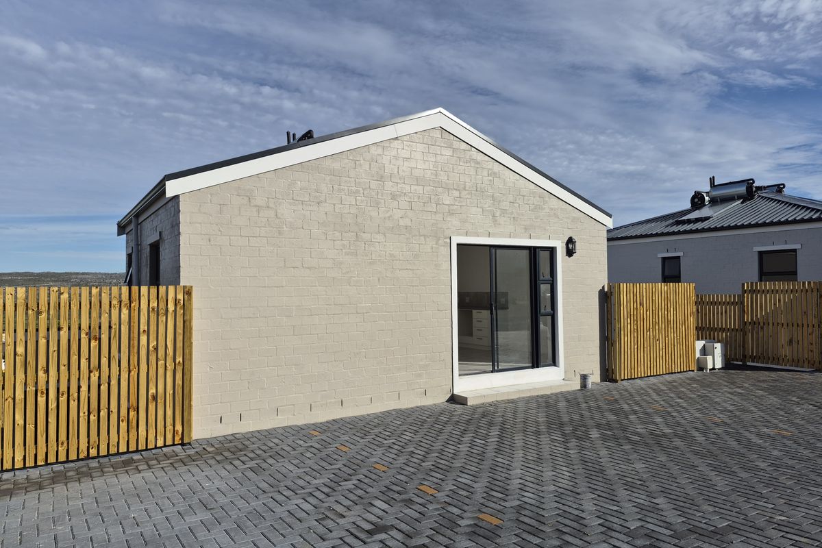 A modern rear exterior view of the apartment featuring a painted brick facade, paved driveway, and timber slat fencing.